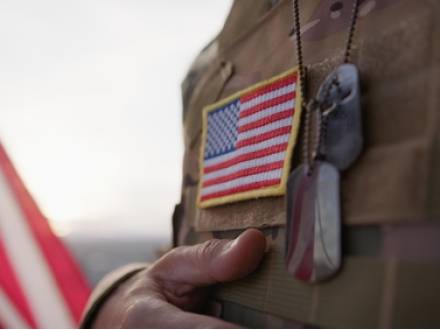 A soldier displays an American flag while holding a dog tag